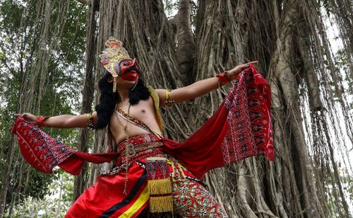 Free Masked dancer in vibrant costume performs under a large banyan tree in Yogyakarta, Indonesia. Stock Photo