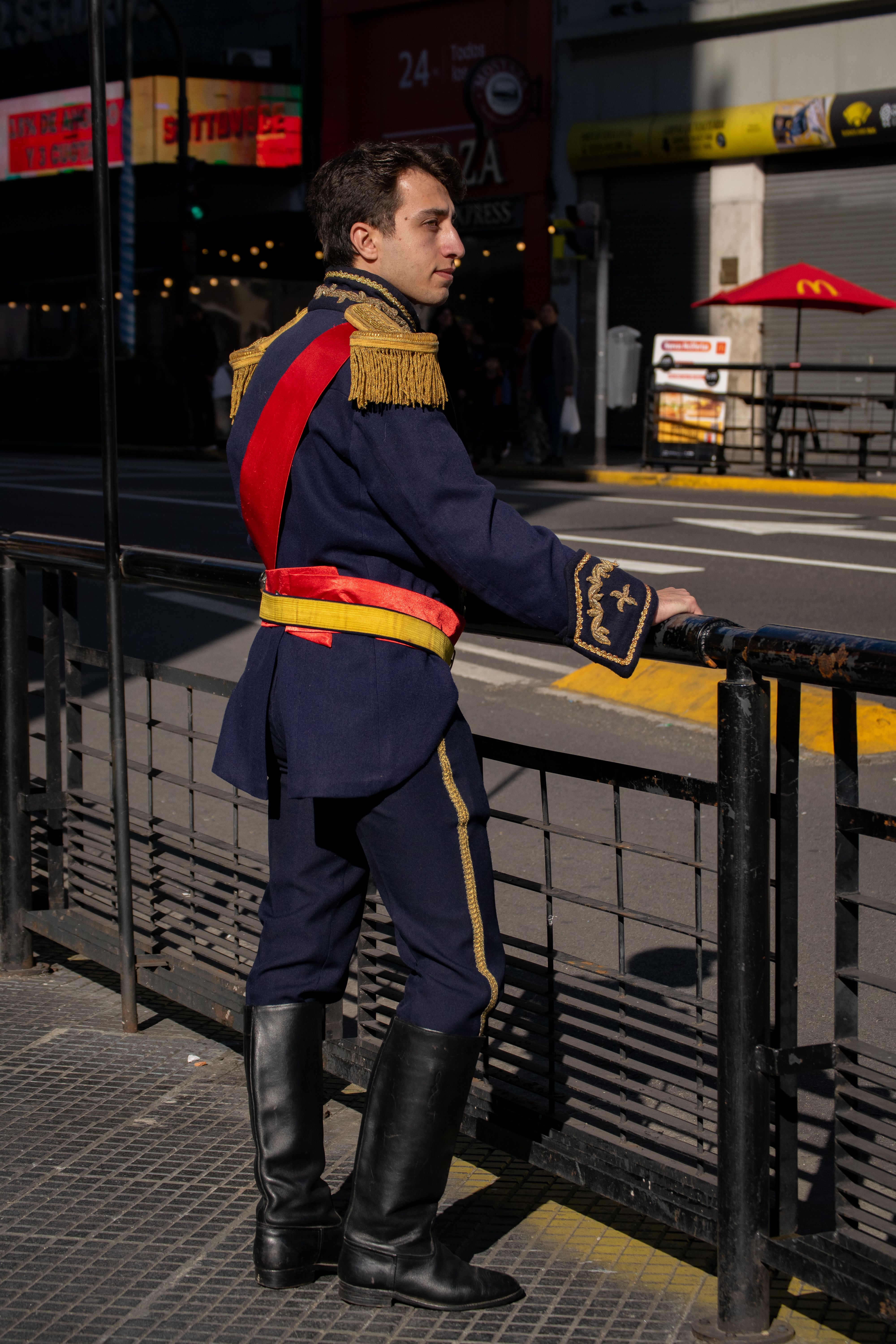 Man in vintage military uniform stands by railing on a city street in daylight.