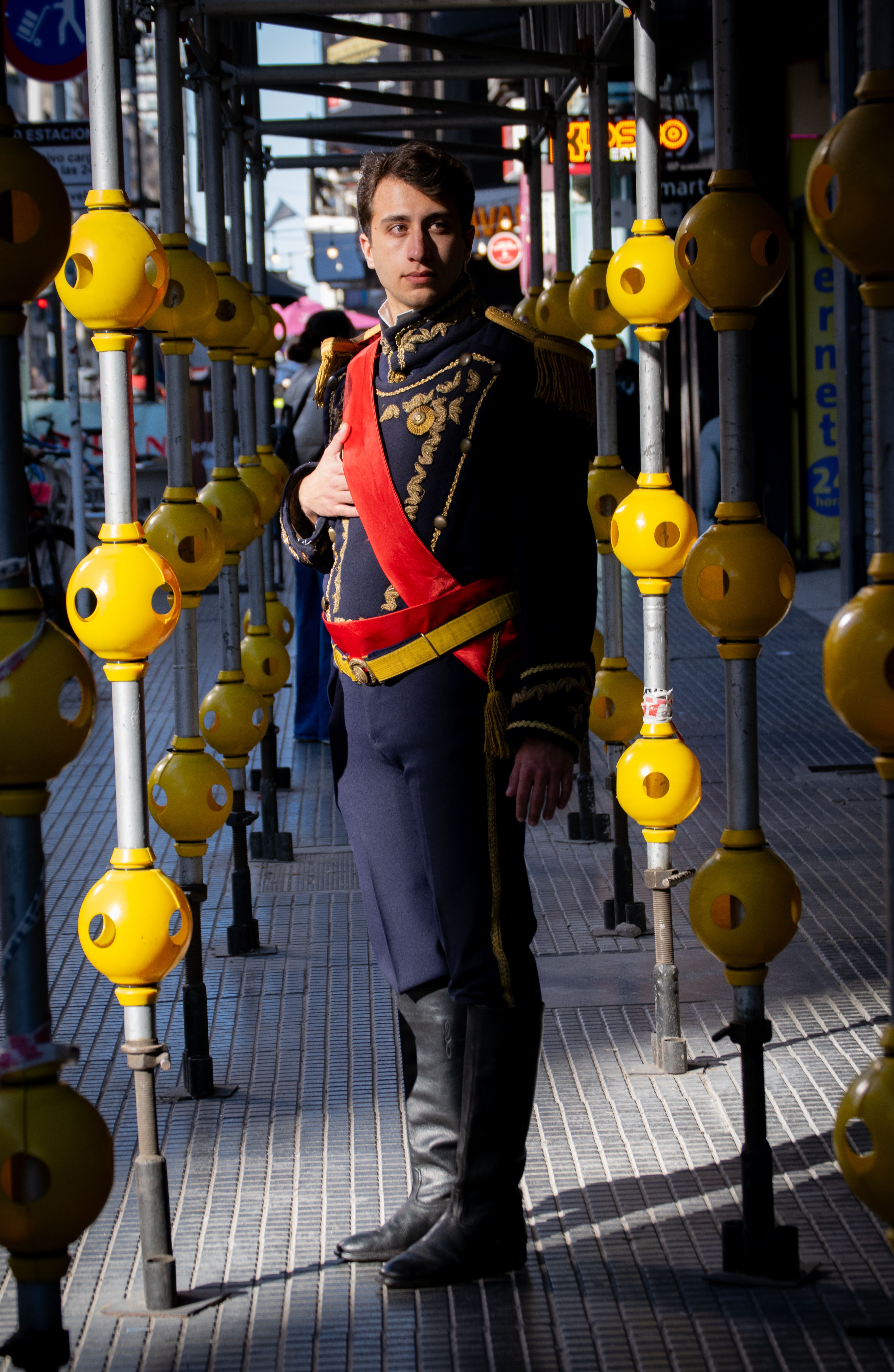 A man dressed in historical military attire stands confidently on an urban street.