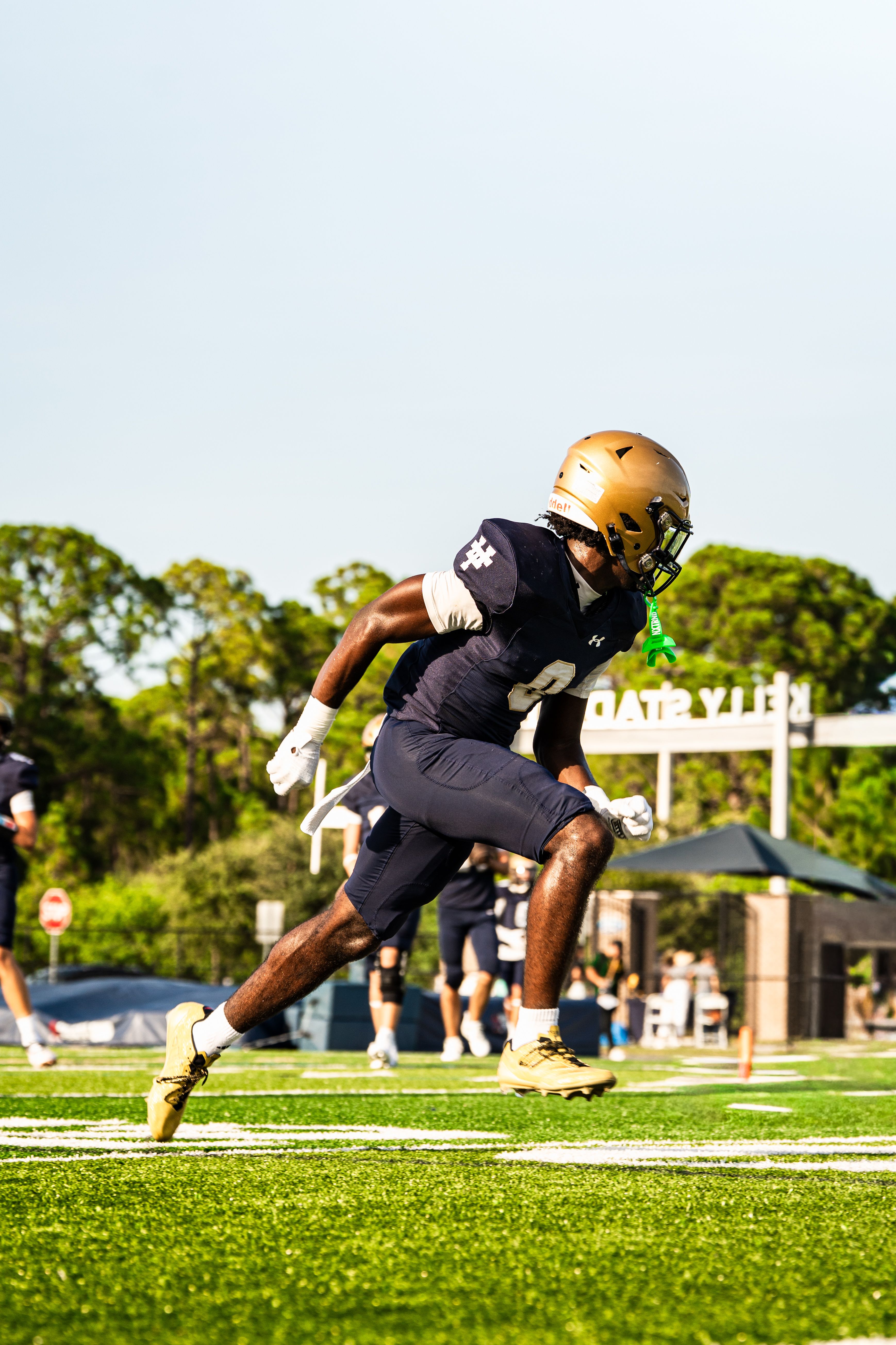 Football player running on a field during a bright day outdoors.