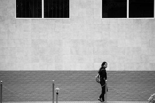 Free Black and white photo of a person walking by a textured wall, capturing city life. Stock Photo