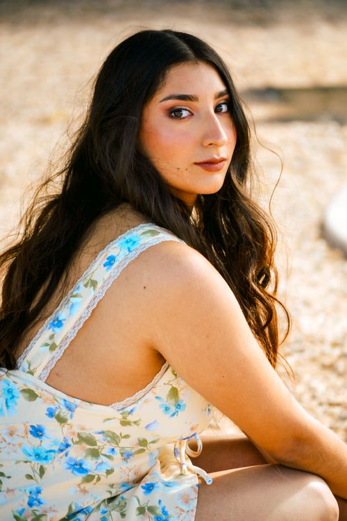 Free A woman in a floral dress poses outdoors under bright sunlight, showcasing natural beauty. Stock Photo