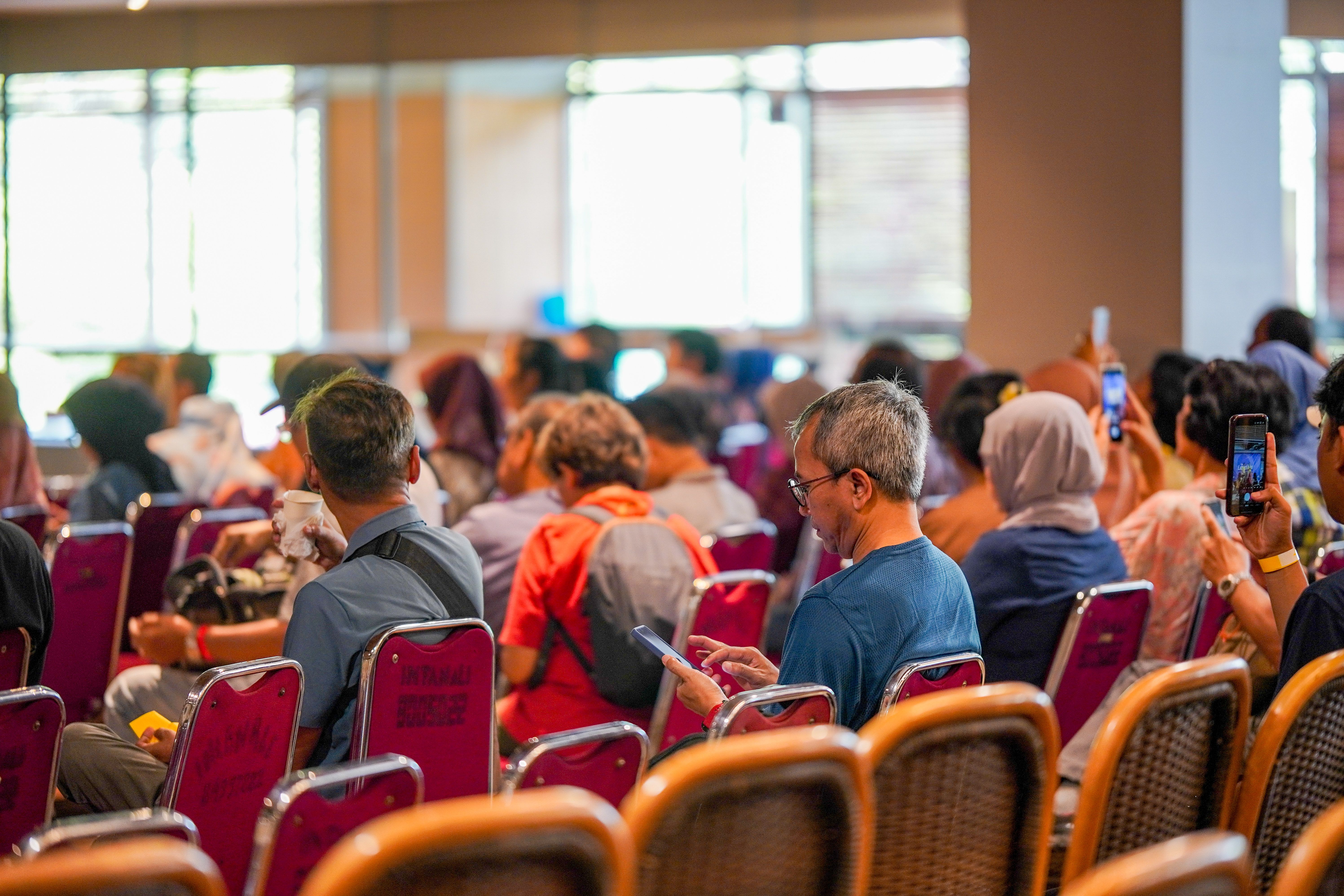 A group of adults at a conference in Jakarta using mobile devices in a vibrant atmosphere.