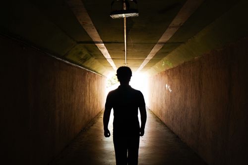 Free A silhouette of a person walking towards the light at the end of a tunnel. Stock Photo