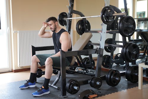 Man in Black Tank Top and Black Shorts Sitting on Black Exercise Bench