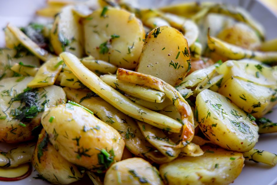A bowl of chunky yellow potato salad with visible celery, red onion, chopped egg, and flecks of fresh dill in a creamy dressing.