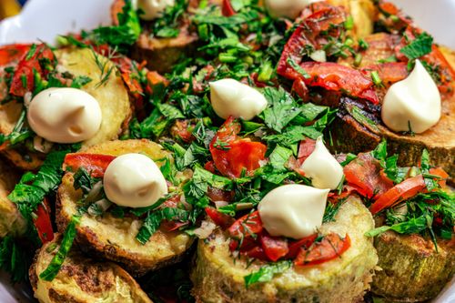Free Deliciously garnished fried vegetables topped with fresh herbs and dollops of sauce. Vibrant food photography. Stock Photo