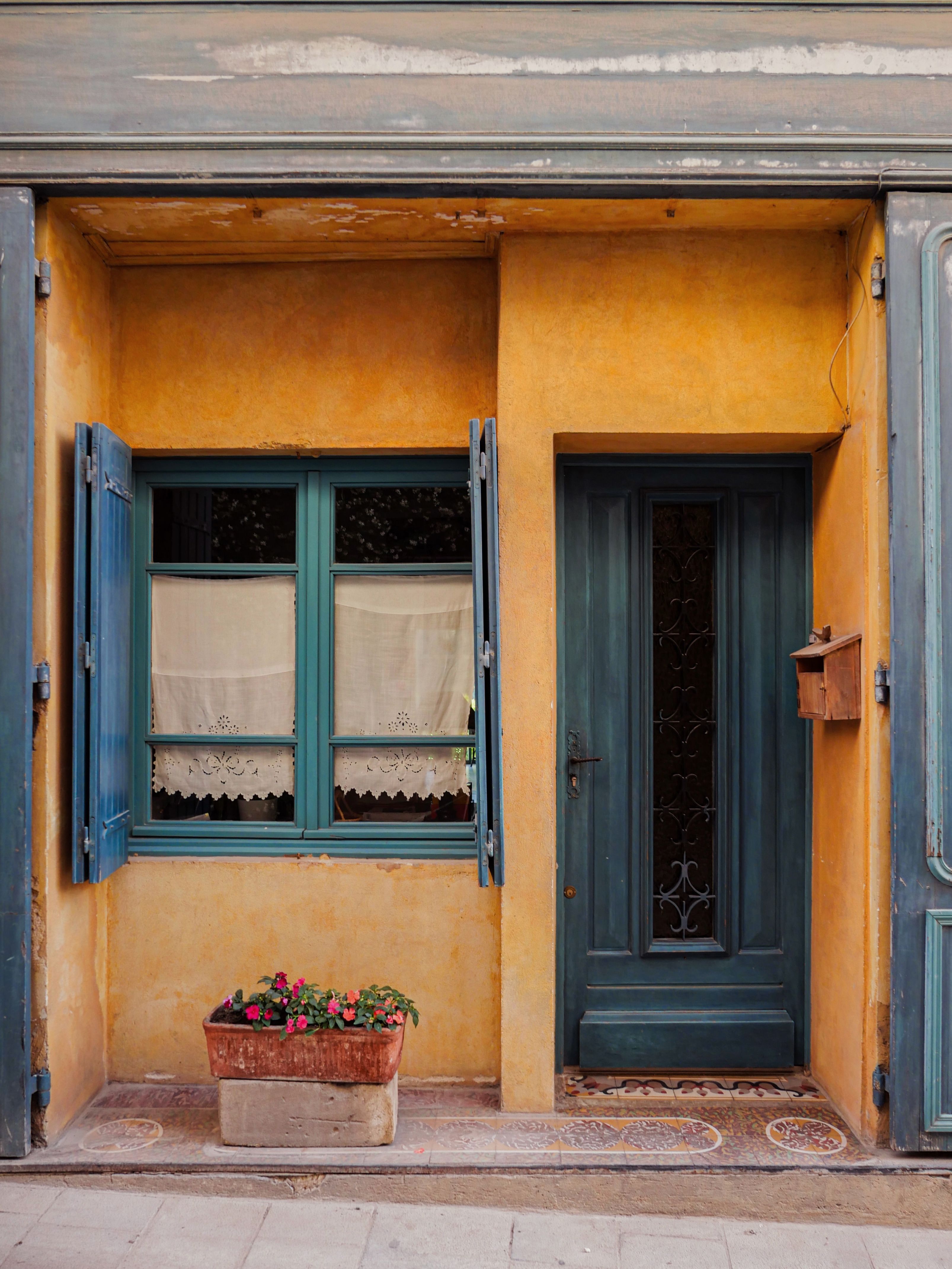 Rustic doorway in Provence, featuring blue shutters and vibrant flowers.