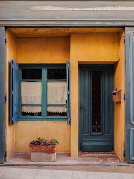 Rustic doorway in Provence, featuring blue shutters and vibrant flowers.