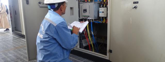 Engineer in uniform inspecting an electrical control panel in an industrial setting.