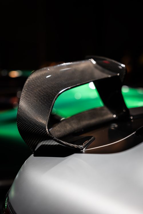 Free Detailed view of a carbon fiber spoiler on a sleek car under showroom lights. Stock Photo