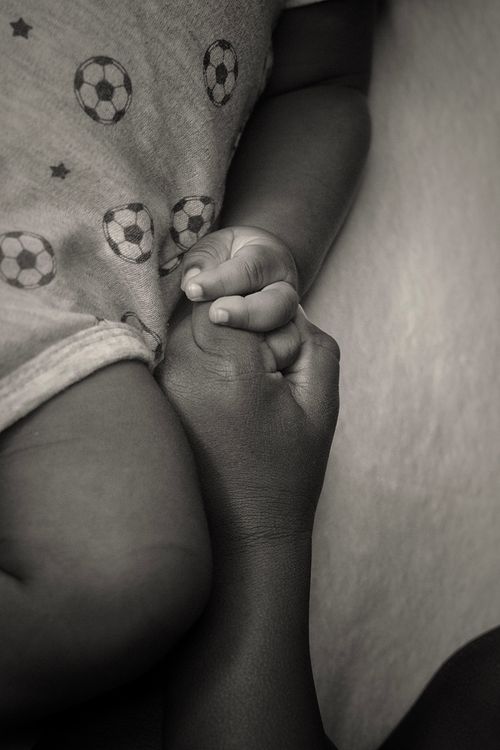 Free A touching black-and-white photo of a baby's hand holding an adult's finger, symbolizing love and connection. Stock Photo