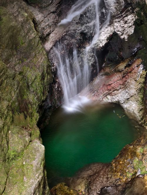 Free Captivating waterfall plunging into a vibrant emerald pool nestled among rocky cliffs. Stock Photo