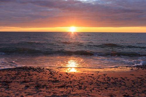Free Beautiful sunset over ocean waves with a tranquil sandy beach foreground. Stock Photo