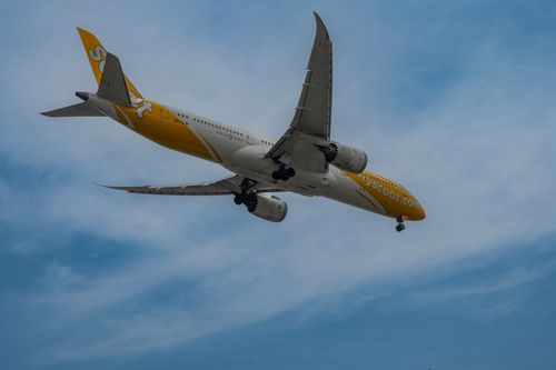 Free A yellow and white airplane flying overhead against a clear blue sky, showcasing its wings and engines. Stock Photo