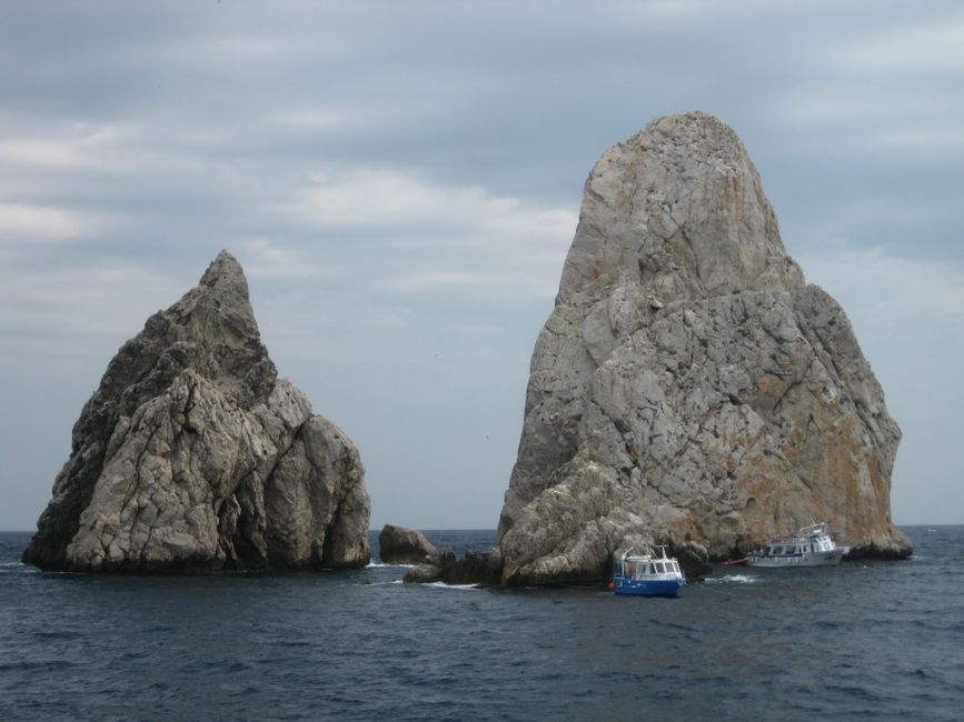 Two striking rock formations rise from the sea, framed by a cloudy sky.