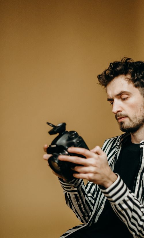 Free Portrait of a male photographer adjusting a DSLR camera indoors with a neutral background. Stock Photo