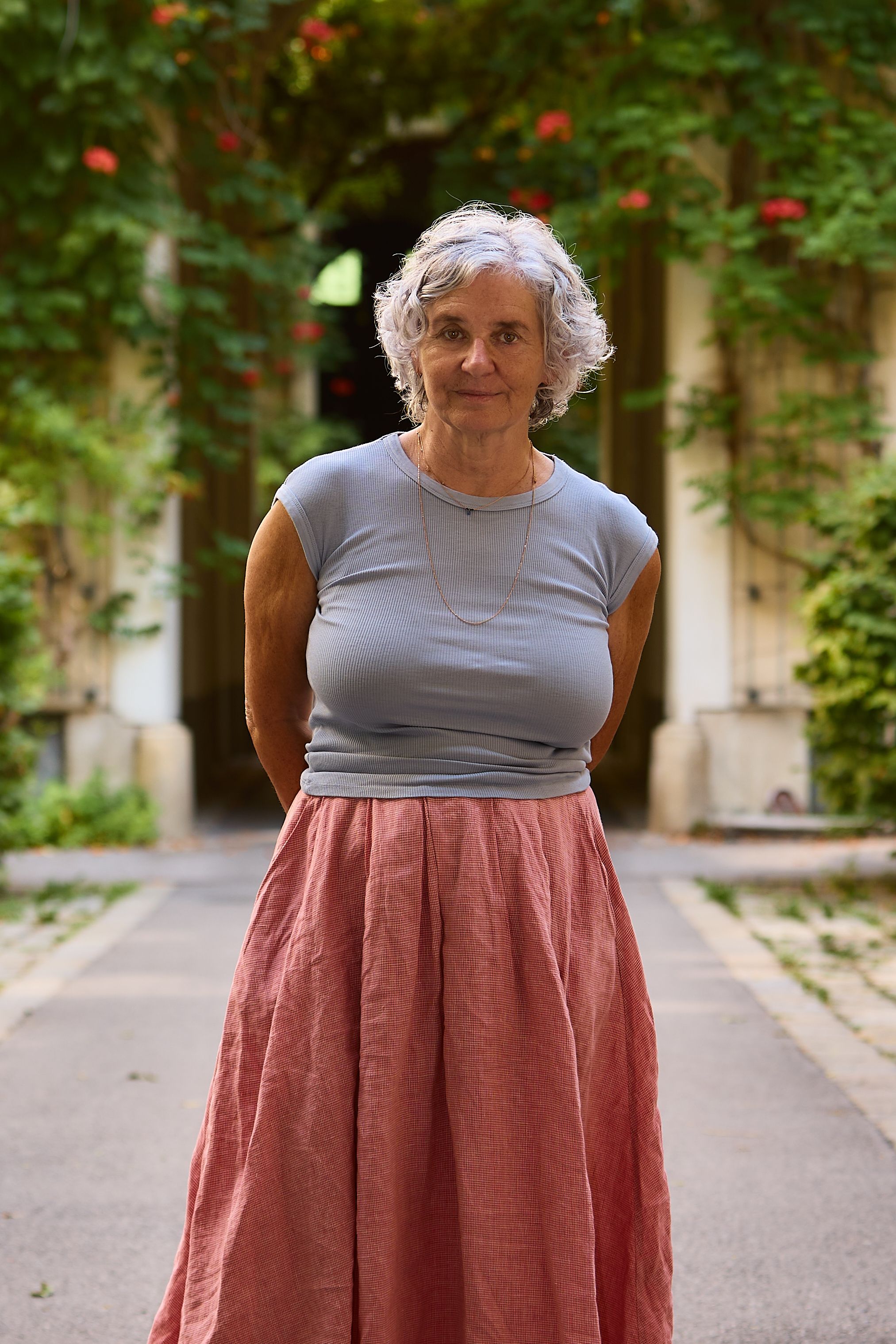 Senior woman standing outdoors with greenery background.