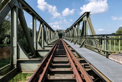 Free A rustic metal bridge with railroad tracks stretching into the distance under a clear sky. Stock Photo