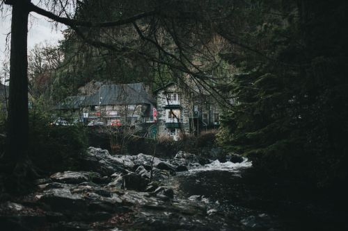 Free Rustic stone house nestled in lush forest alongside a flowing river in Wales, UK. Stock Photo