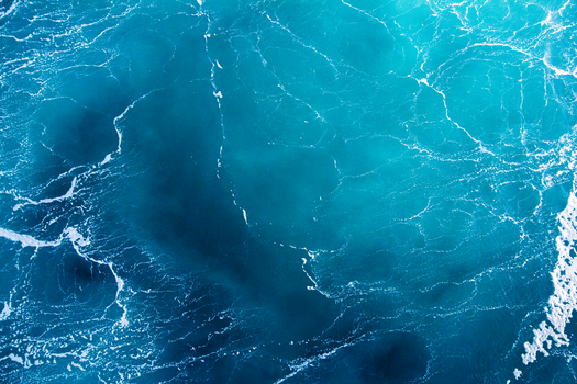 Vivid aerial shot of turquoise ocean waves creating intricate patterns, conveying a sense of serenity and natural beauty.