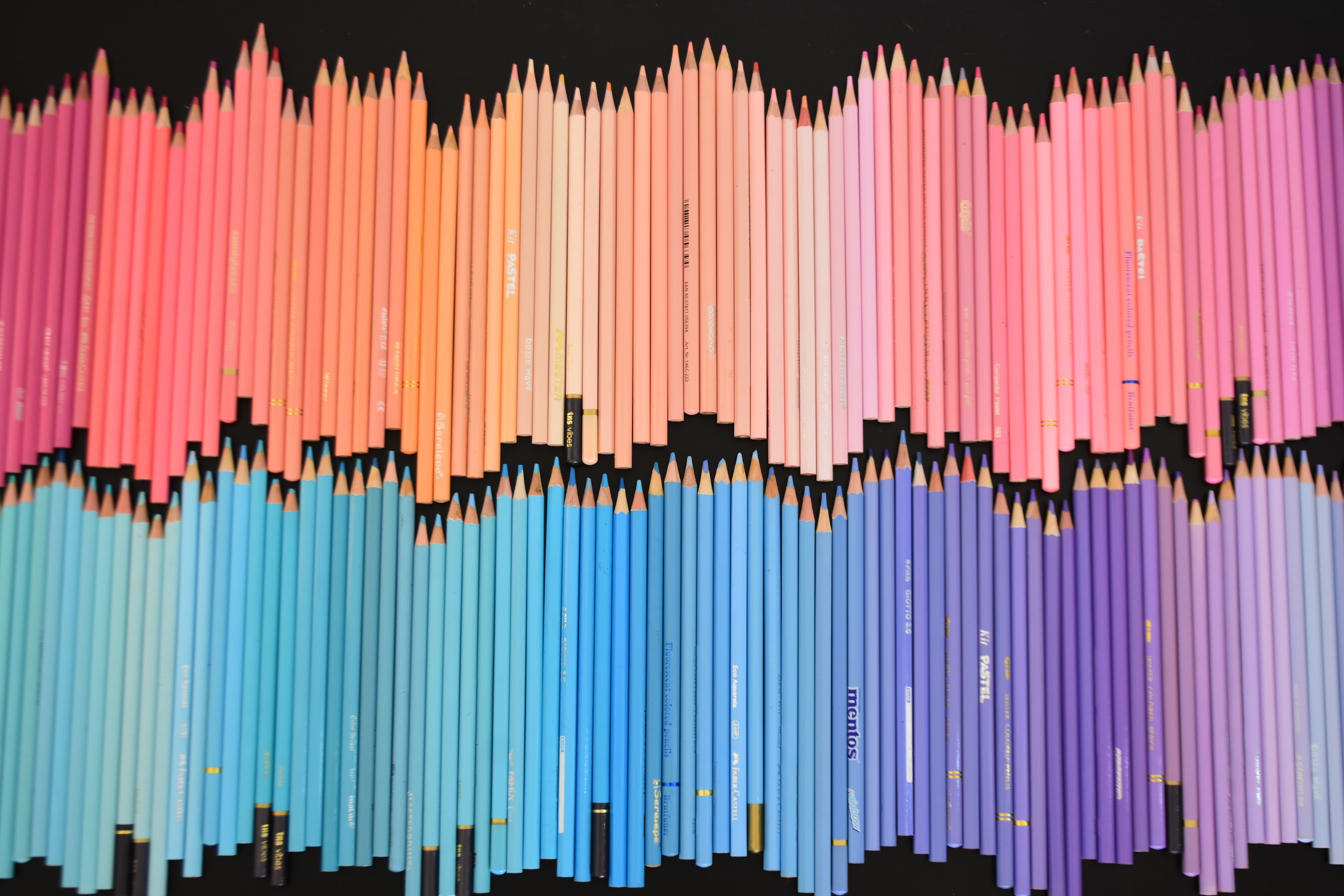 Uma vibrante composição de lápis multicoloridos dispostos em um padrão degradê sobre um fundo preto.