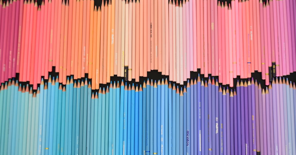 Uma vibrante composição de lápis multicoloridos dispostos em um padrão degradê sobre um fundo preto.