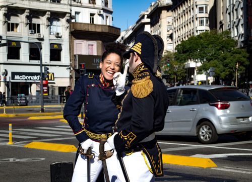 Free Two historical reenactors in uniform share a laugh on a busy urban street with cars passing by. Stock Photo