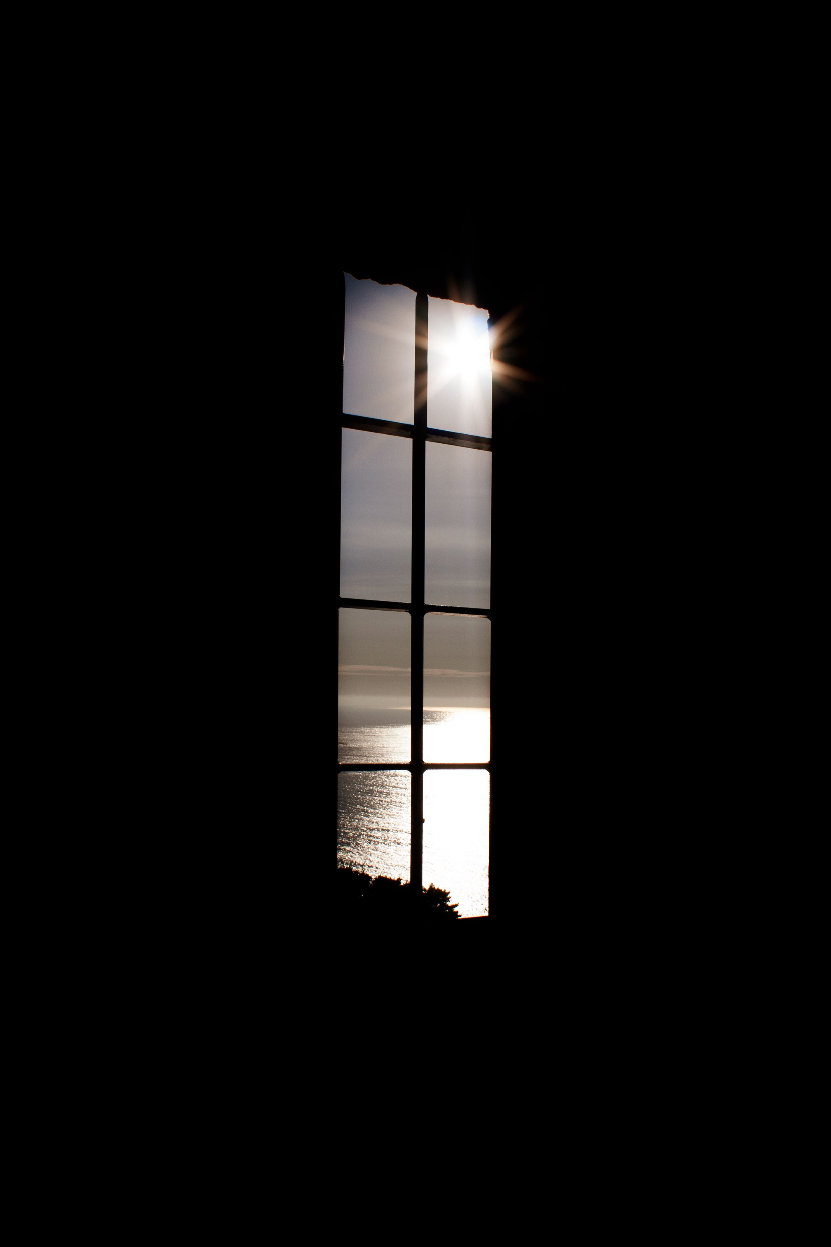 Sunlight streams through a tall window, casting a glow on the ocean view