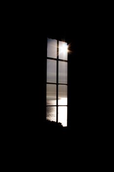 Sunlight streams through a tall window, casting a glow on the ocean view