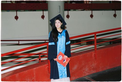Free A young female graduate in cap and gown stands proudly holding her diploma indoors. Stock Photo