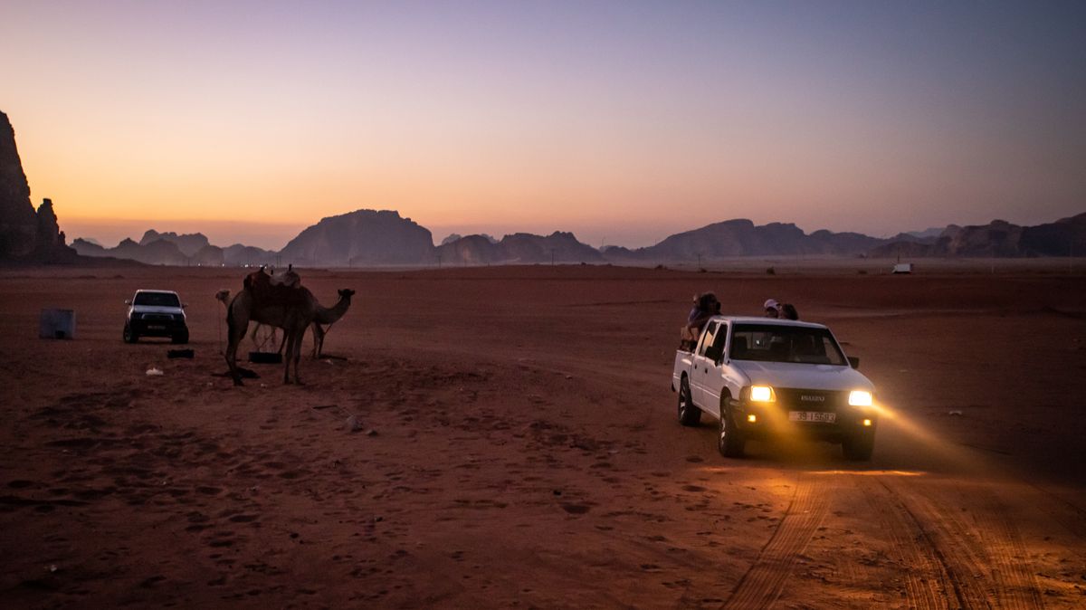 Nightfall in Wadi Rum showcasing camels and vehicles set against a stunning desert backdrop.