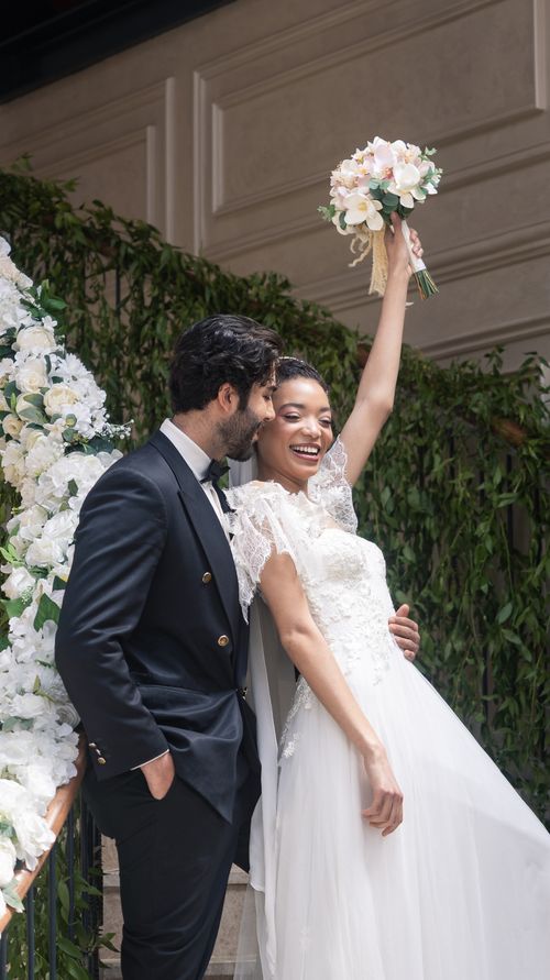 Free A newlywed couple joyfully celebrating on an elegant, floral-decorated staircase. Stock Photo
