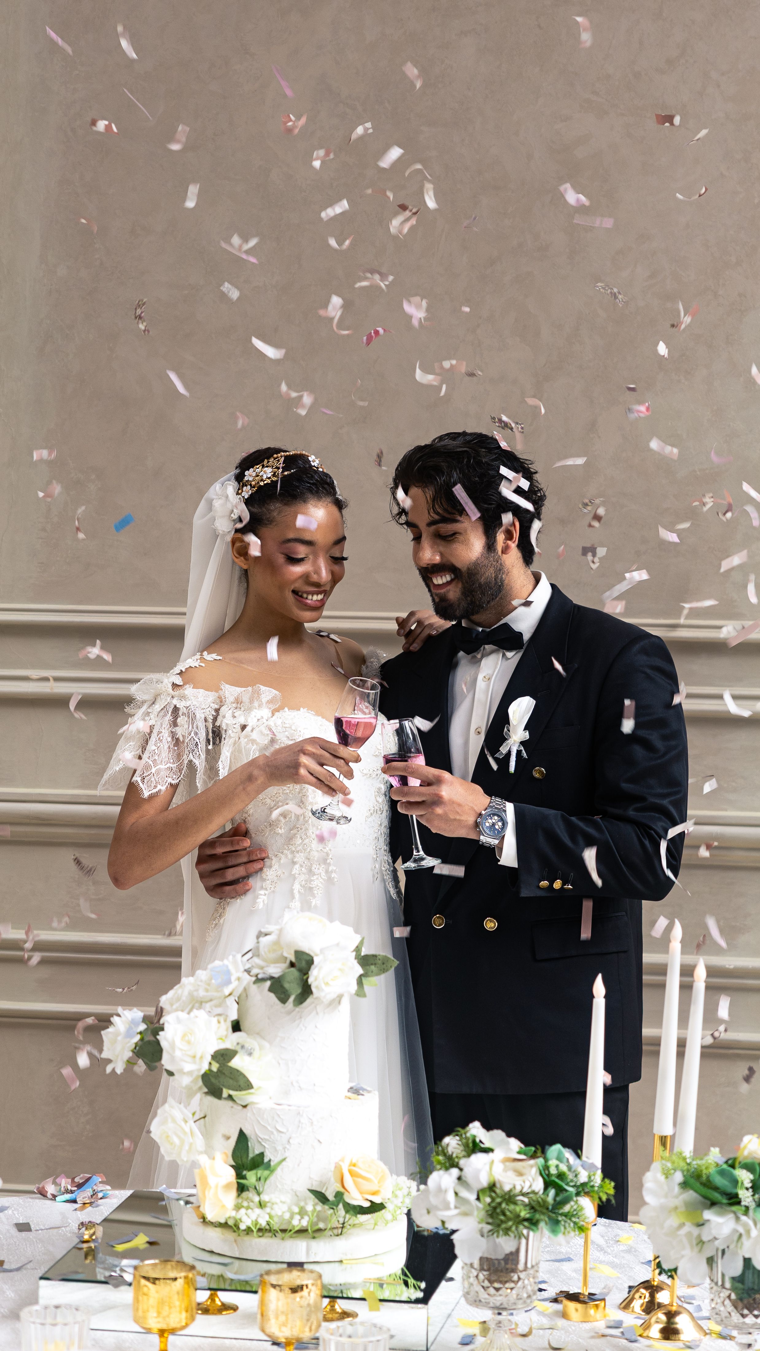 Newlyweds celebrating with a wedding cake amidst confetti indoors.