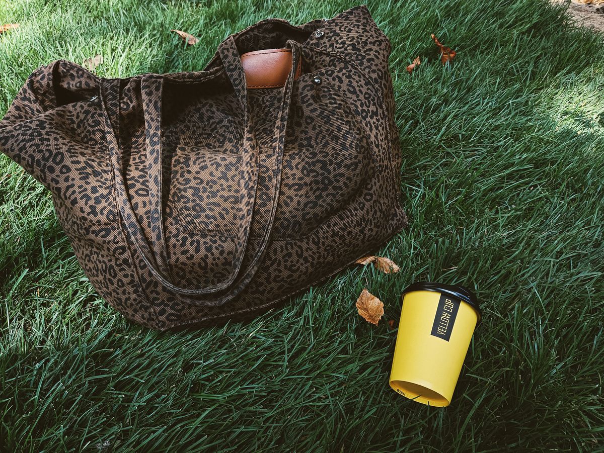 Leopard print canvas tote bag styled on autumn grass with fallen leaves and a coffee cup