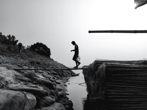 A striking black and white silhouette of a man crossing a narrow bridge at dusk, reflecting solitude.