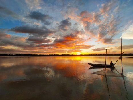 A peaceful sunset scene over a lake with a lone fisherman in a boat, surrounded by vibrant clouds.