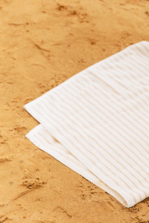 Free A crisp white striped towel lies neatly on a golden sandy beach, ready for a relaxing summer day. Stock Photo