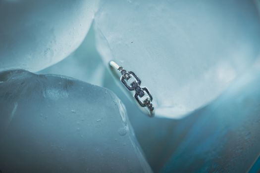 Close-up of a silver ring resting on ice, showcasing intricate detail and cold tones.