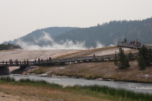 Visitors walk along boardwalk near steaming geysers in Yellowstone.