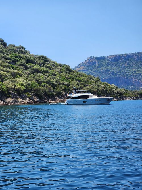 Free A luxury yacht sails on calm waters against a backdrop of lush green hills under a clear blue sky. Stock Photo