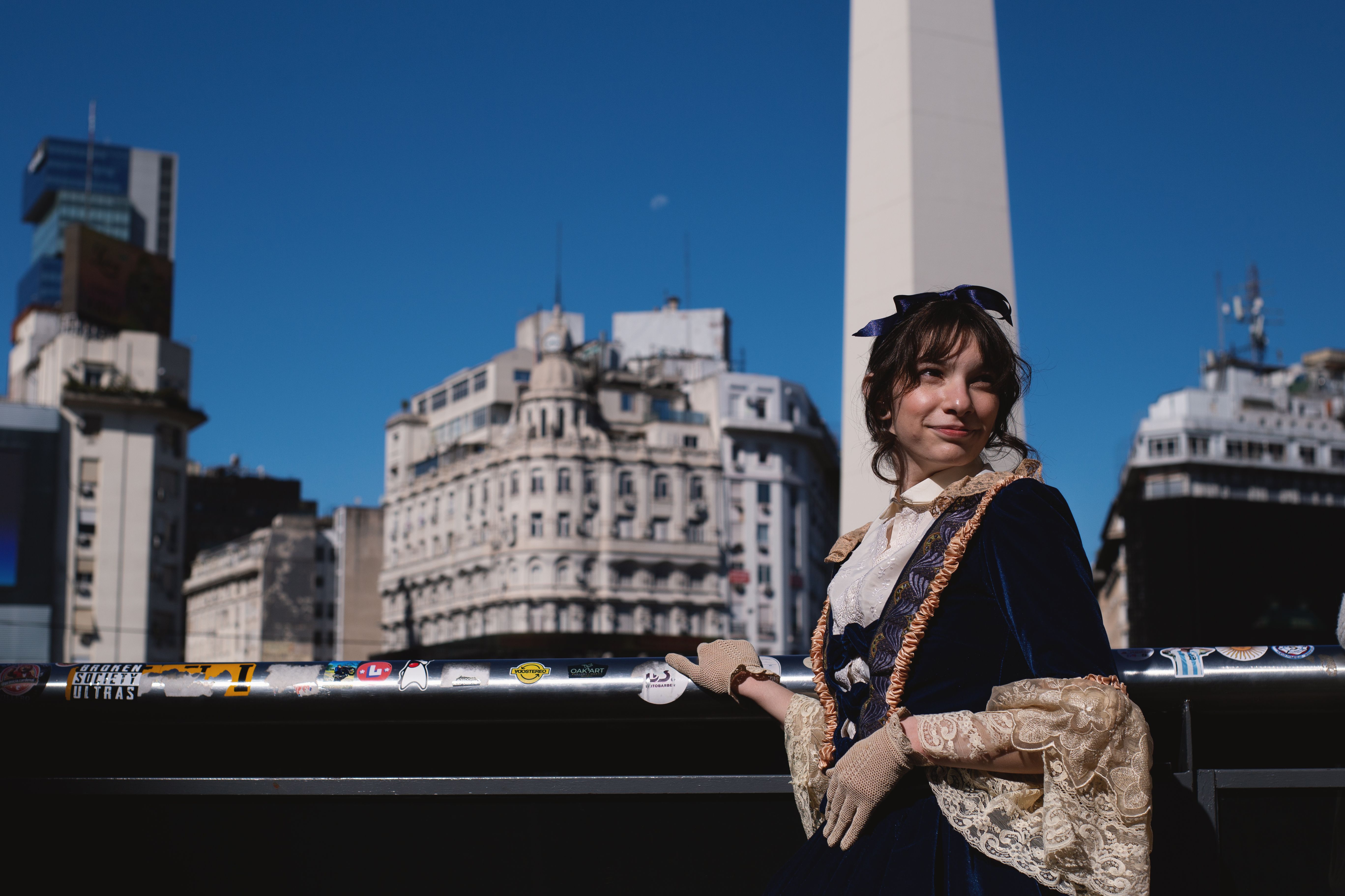 A woman in a vintage dress poses by the Obelisk monument in Buenos Aires under clear blue skies.