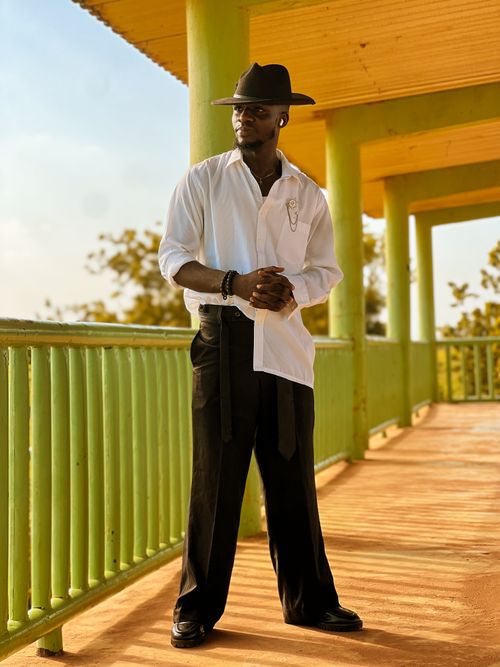 Free Confident man in a white shirt and hat poses under a vibrant yellow structure in daylight. Stock Photo