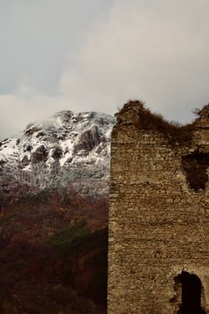 A stone ruin stands tall against a snow-covered mountain in a winter landscape.