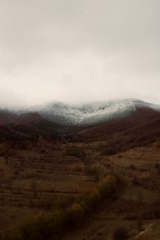 Snow-covered mountain peaks with cloudy sky above, autumn landscape.