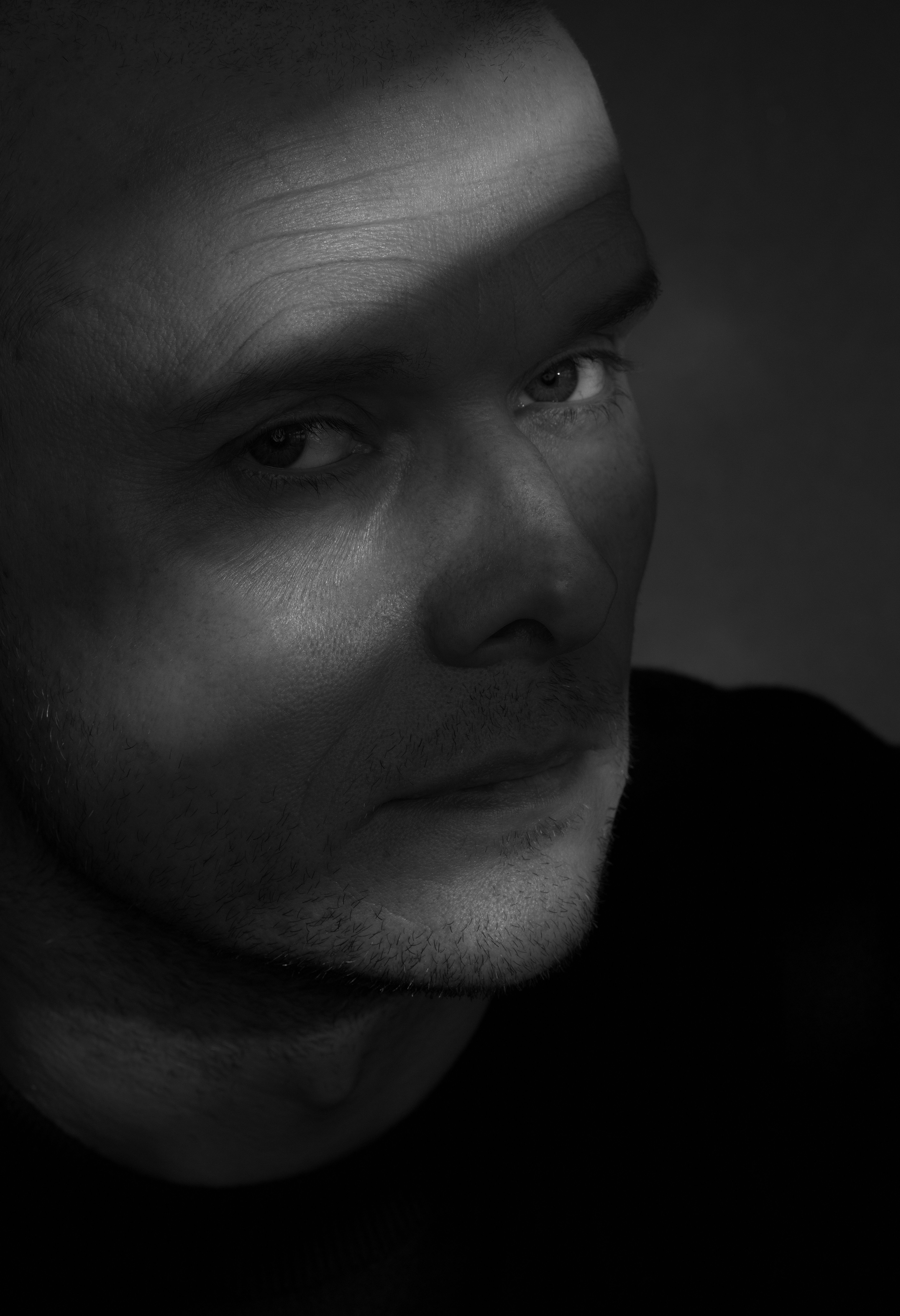 Moody black and white portrait of a man with focused gaze and dramatic lighting.