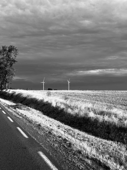 Free Dramatic black and white landscape with road, wind turbines, and cloudy sky. Stock Photo