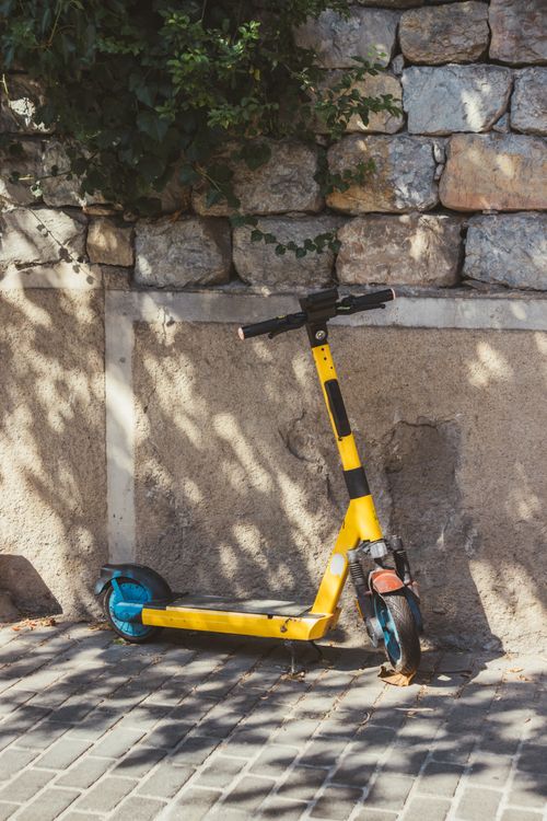 Free A vibrant yellow electric scooter resting against a stone wall on a sunny day. Stock Photo