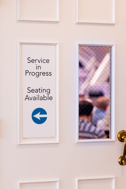 Free White door with sign 'Service in Progress' and a peek into a room with people inside. Stock Photo