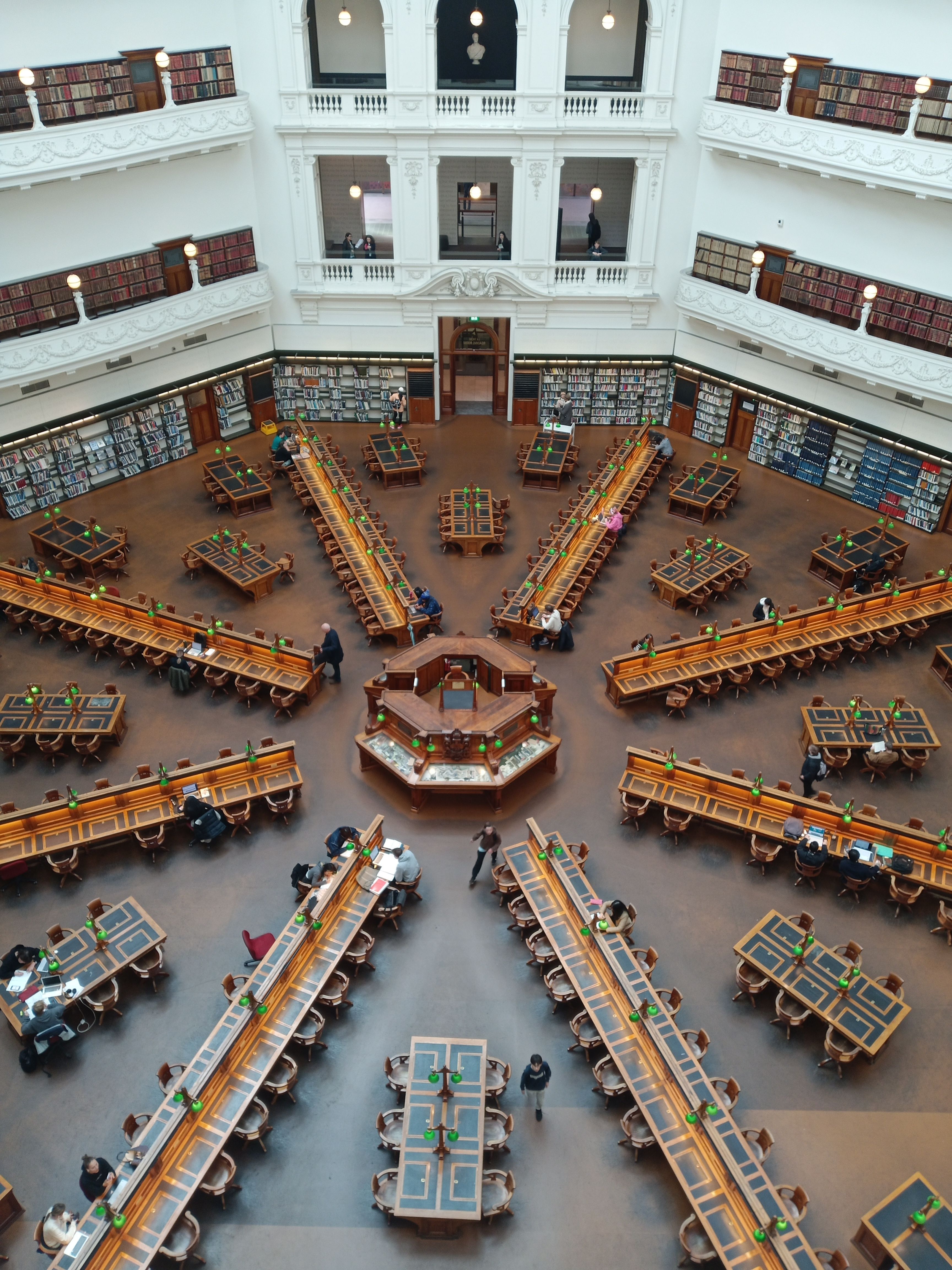 An ornate library interior with large reading tables and bookshelves, viewed from above.
